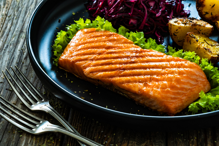 Grilled salmon steak with baked potatoes and red cabbage on black plate on wooden table