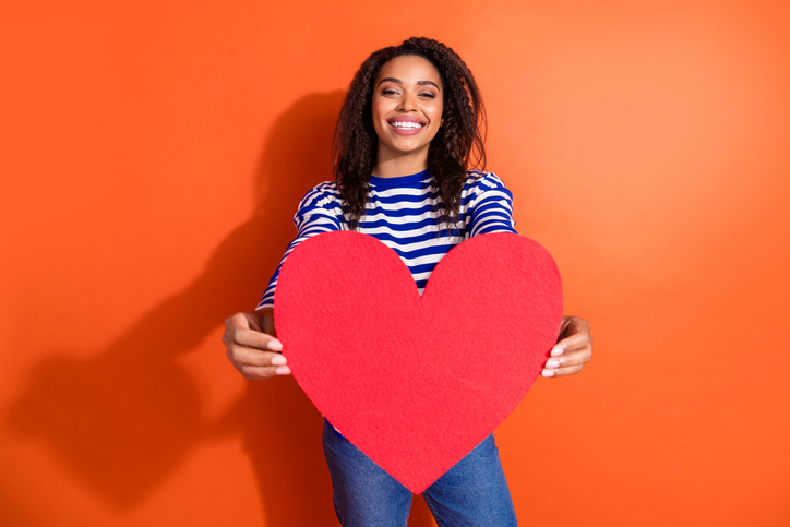 Photo of shiny attractive lady dressed striped shirt showing red heart empty space isolated orange color background